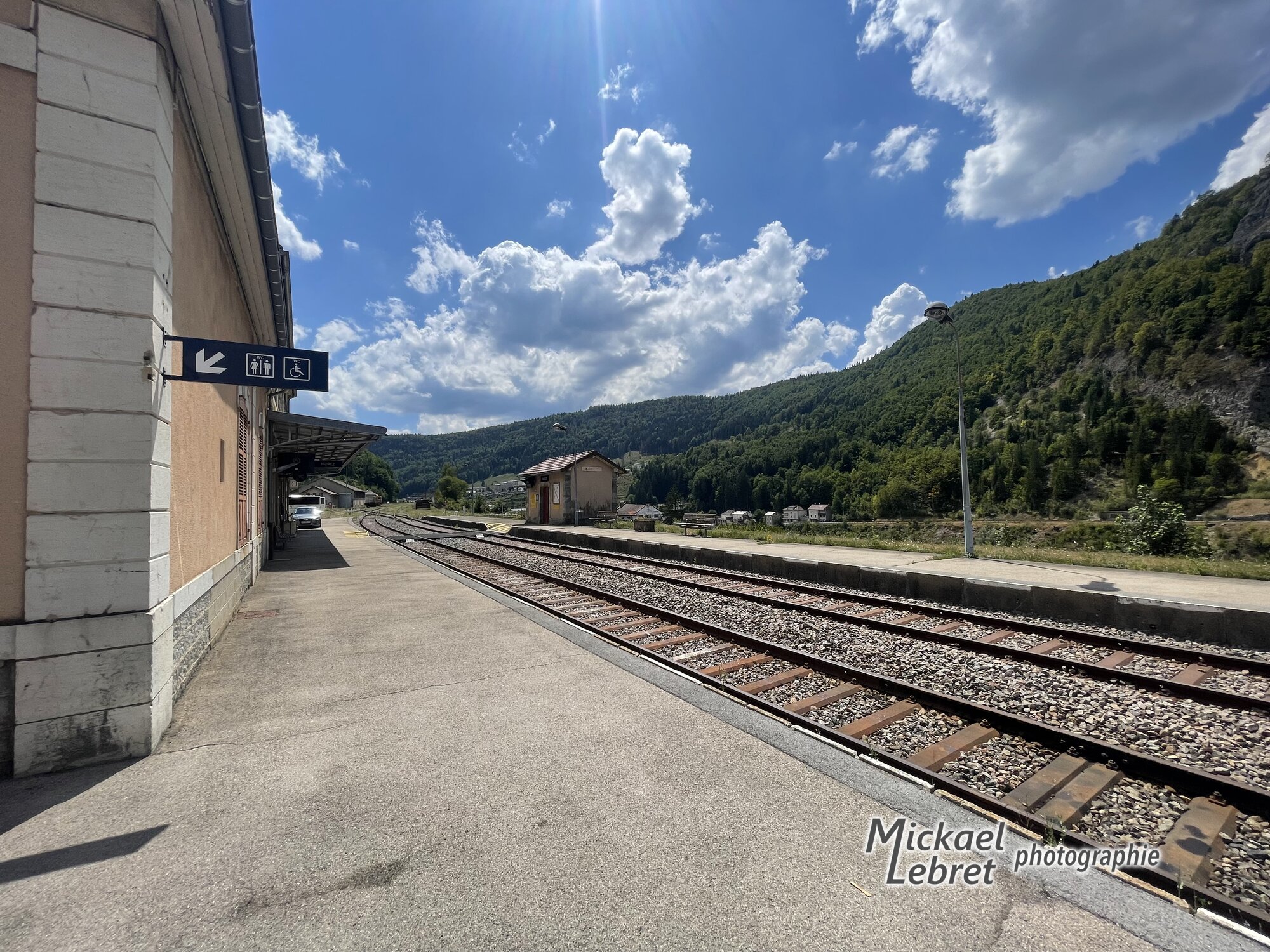Le quai et les voies de la gare de Morez, la montagne boisée en face