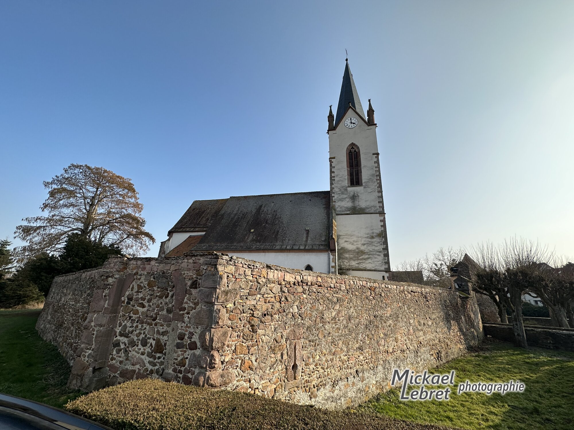 L'église Saint-Blaise derrière l'angle du mur d'enceinte du cimetière fortifié