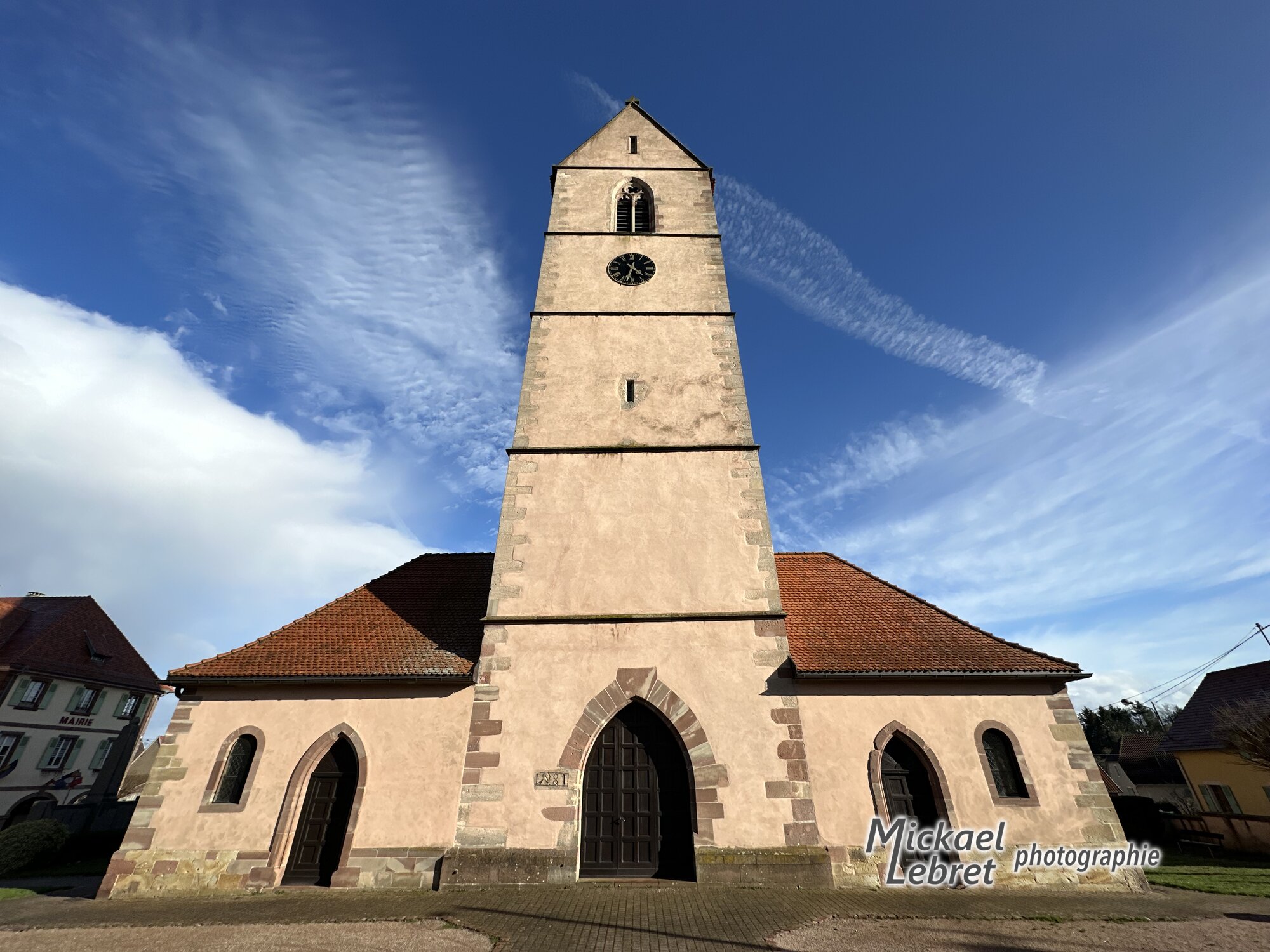 L'église Saint-Jean-Baptiste en contre-plongée, avec sa tour-porche et ses portails en arc brisé